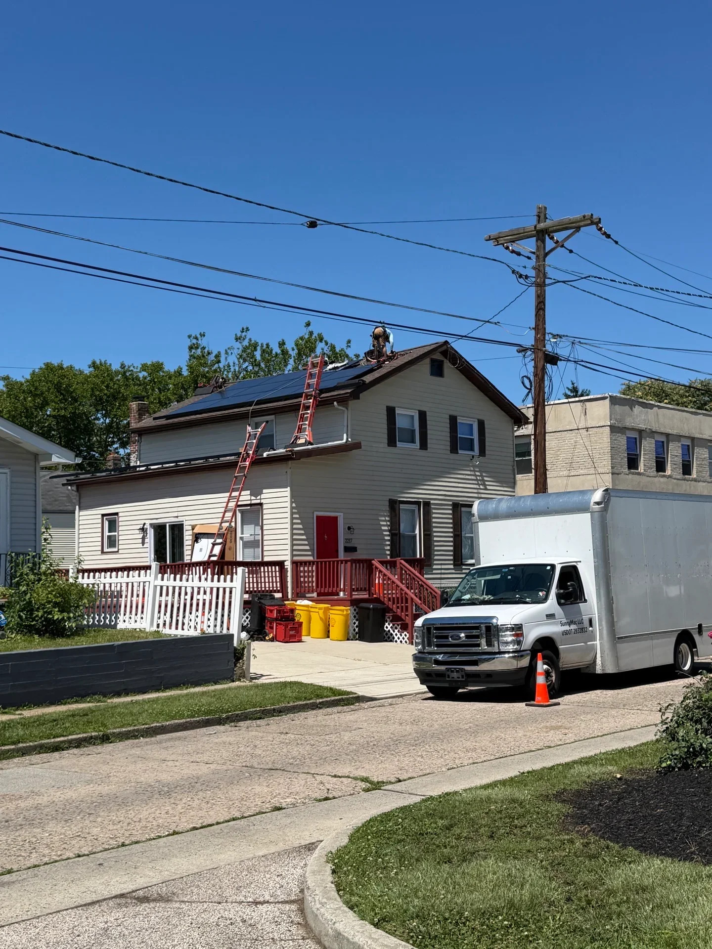 Solar panels installed on residential roof with ladder and service vehicle on driveway
